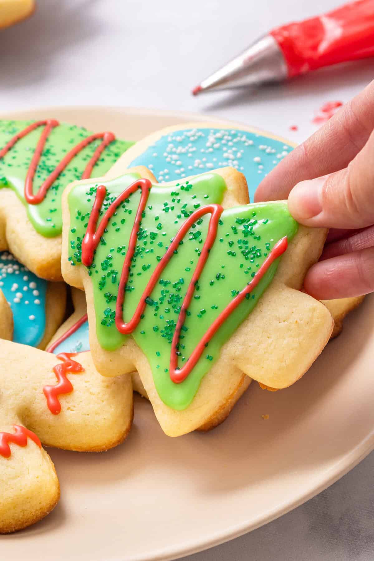 A hand grabbing a cut out Christmas tree cookie covered in sugar cookie icing. 