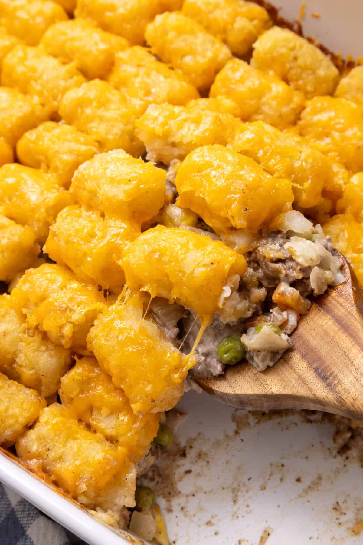 A close up of Tater Tot Casserole being scooped up with a wooden spoon. 