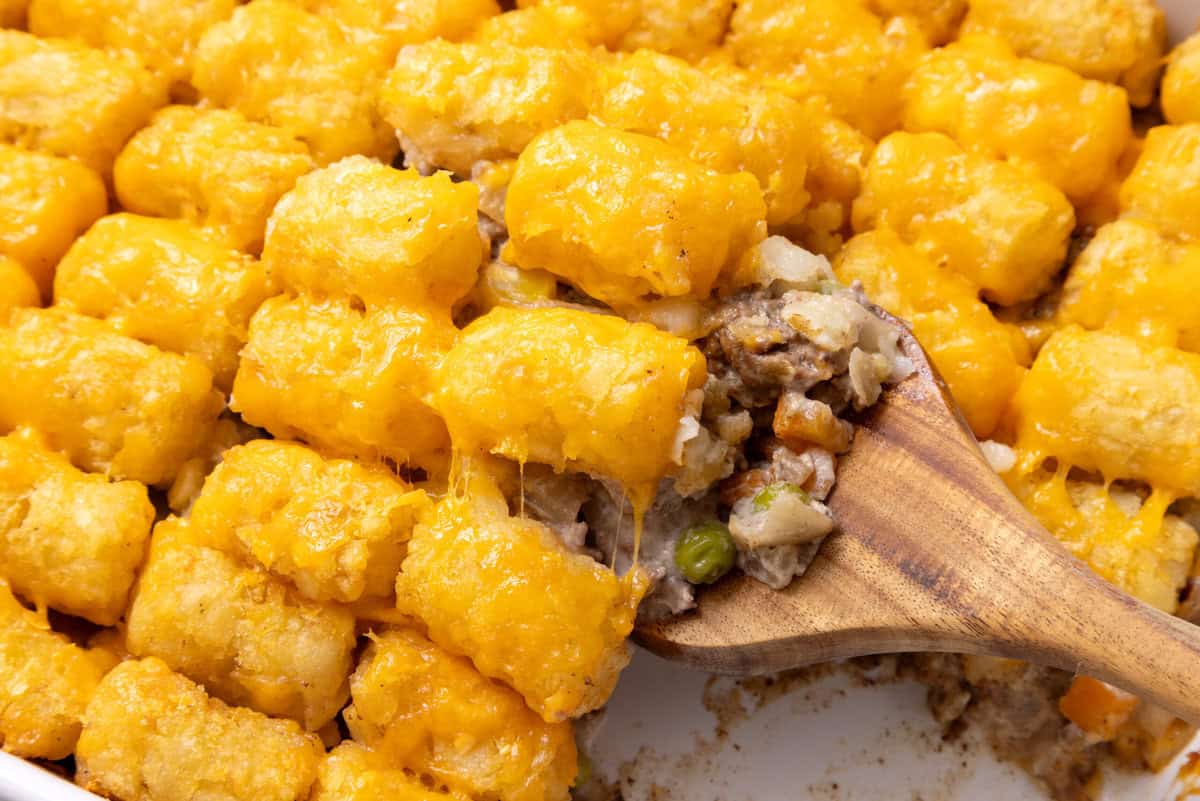 A close up of Tater Tot Casserole being scooped up with a wooden spoon.