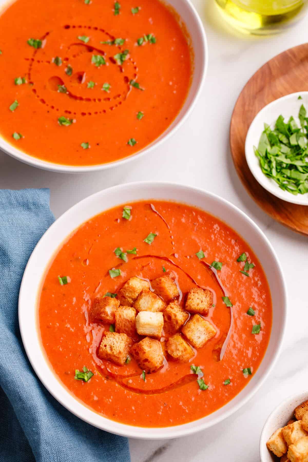 Two bowls of creamy tomato soup with croutons.