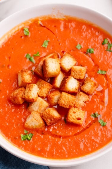 tomato soup in a white bowl with croutons, basil and cream