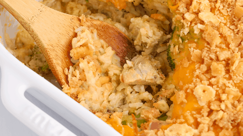 Cheesy chicken and rice casserole with a wooden spoon taking a scoop.