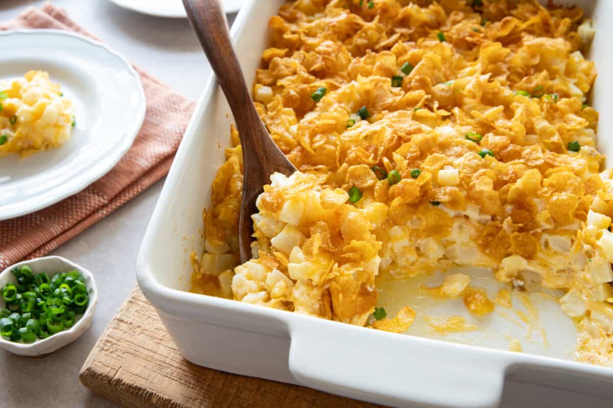 Cheesy potato casserole in baking dish with wooden spoon