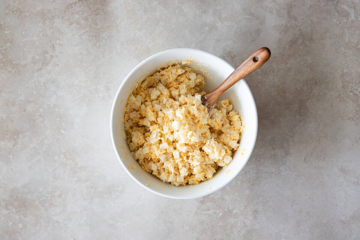 Overhead view of cheesy potato mixture in bowl with wooden spoon