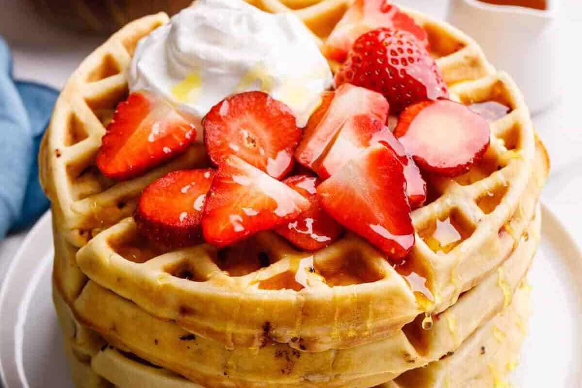 A stack of strawberry waffles topped with fresh strawberries and whipped cream.
