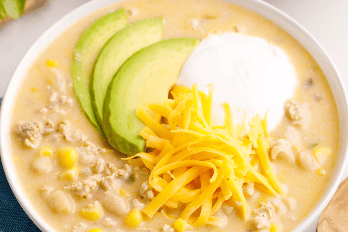 A bowl of white bean chicken chili topped with cheese, yogurt, and avocado slices.