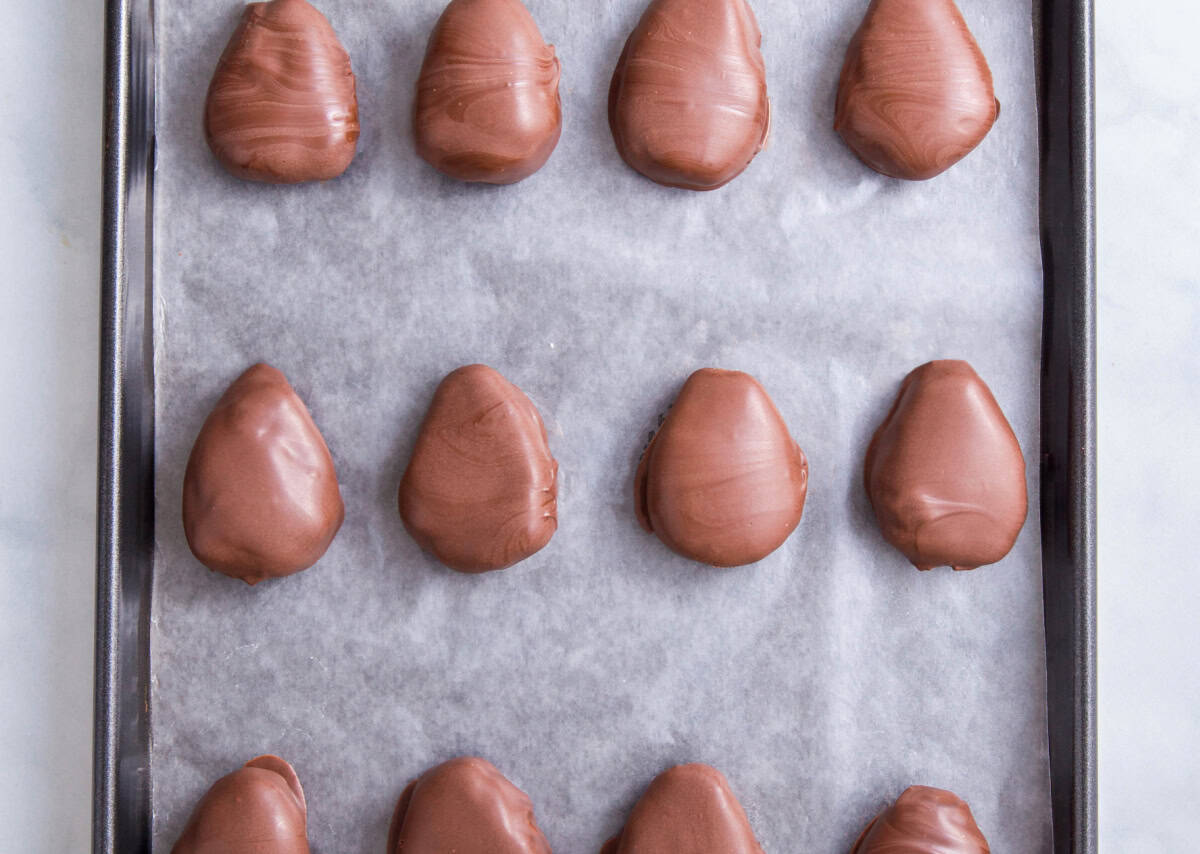 The chilled filling coated in chocolate sitting on top of the lined baking sheet.