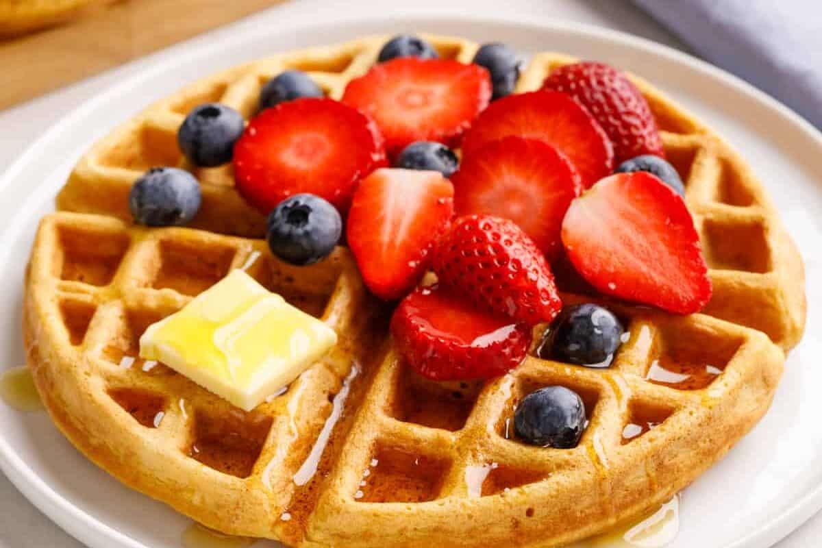A buttermilk waffle topped with strawberries, blueberries, butter, and syrup.