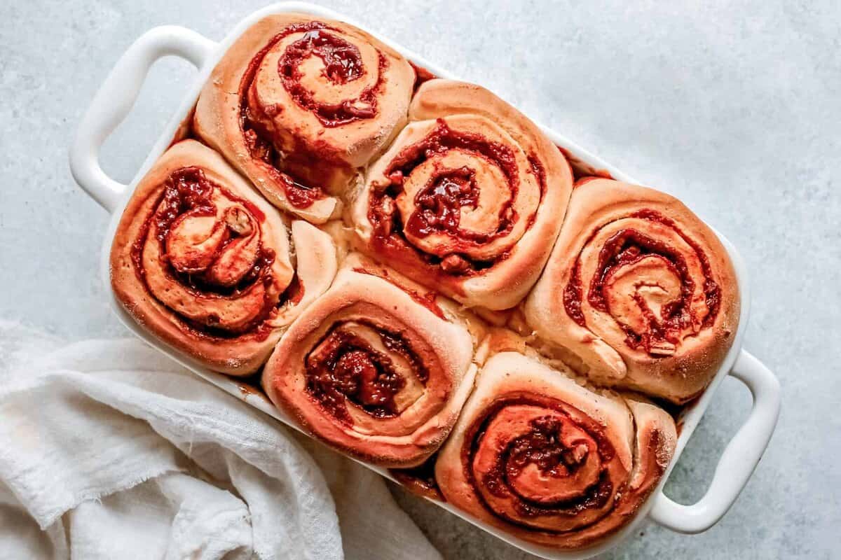 caramel pecan cinnamon rolls in a white casserole dish on a white countertop with a white linen cloth next to the cinnamon rolls