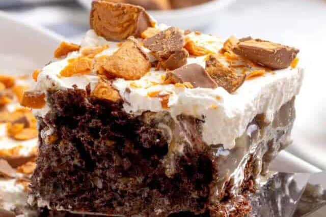 A slice of Butterfinger poke cake being lifted from a pan.