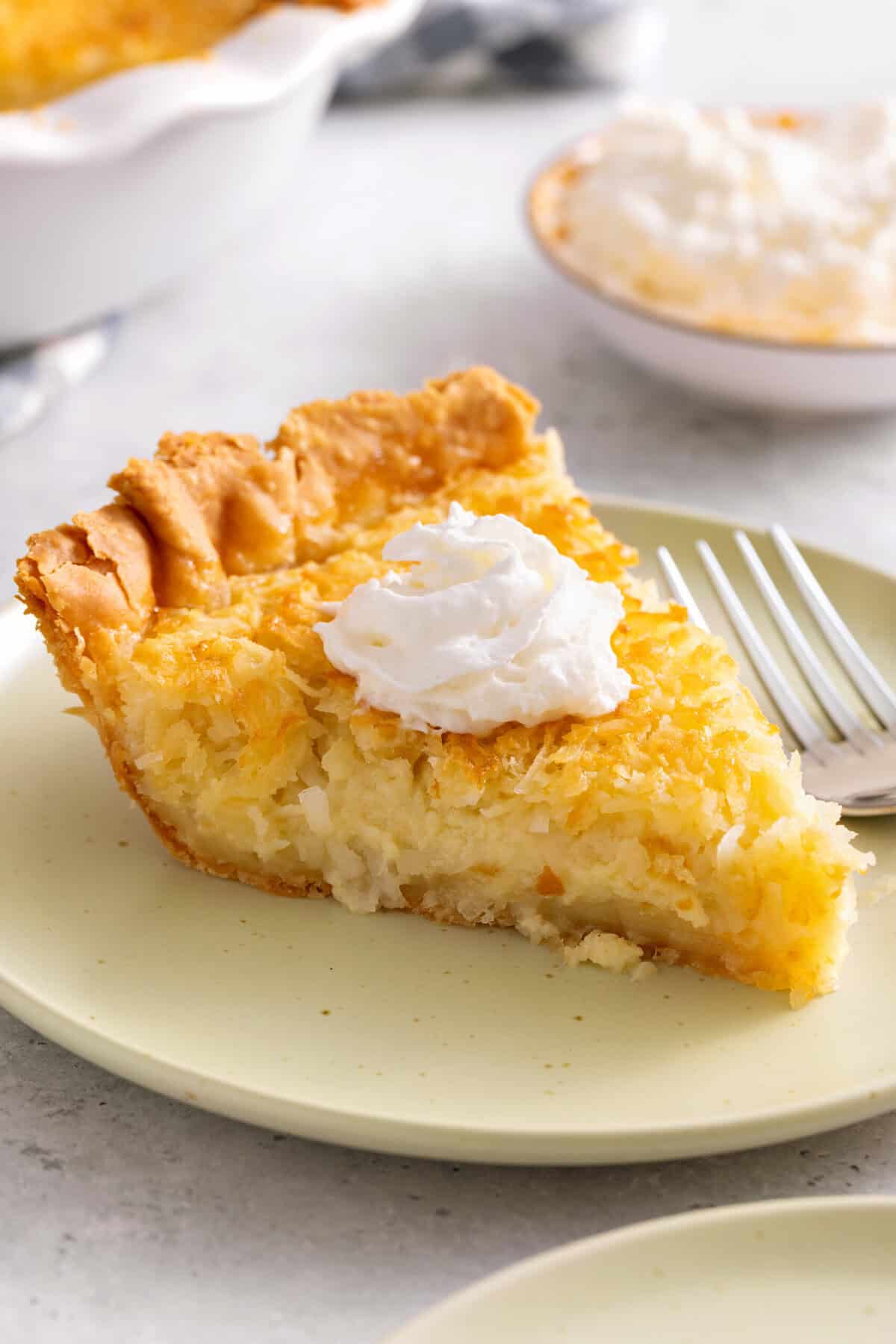 Slice of coconut pie on plate with dollop of whipped cream.