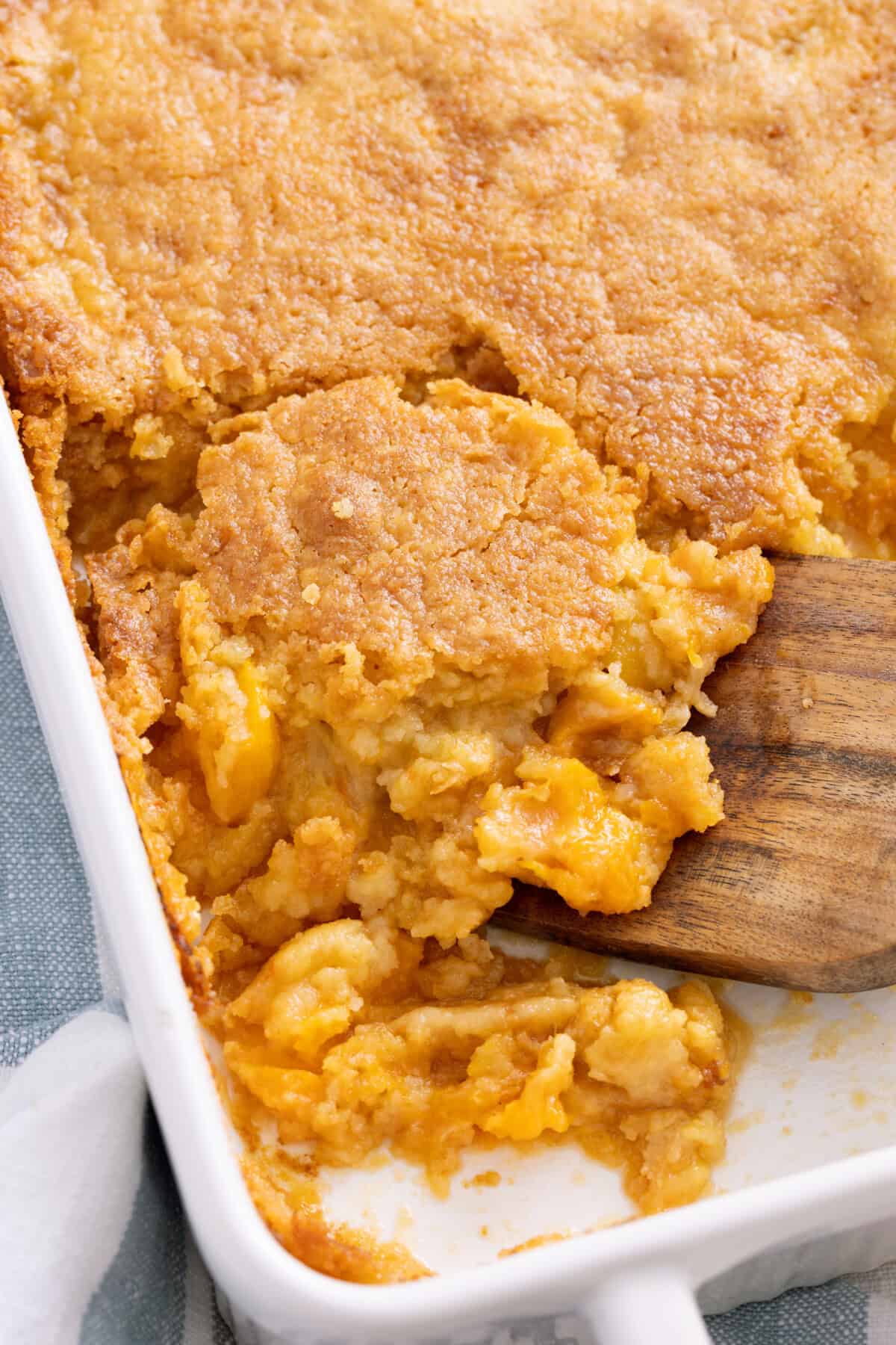 Scooping peach cobbler with baking mix from pan.