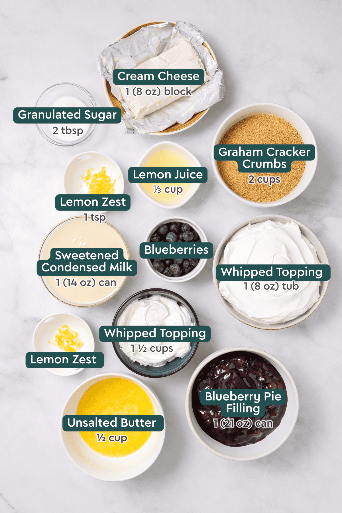 Ingredients for blueberry delight, including cream cheese, sugar, graham crackers, lemon, blueberries, whipped topping, condensed milk, butter, blueberry pie filling.