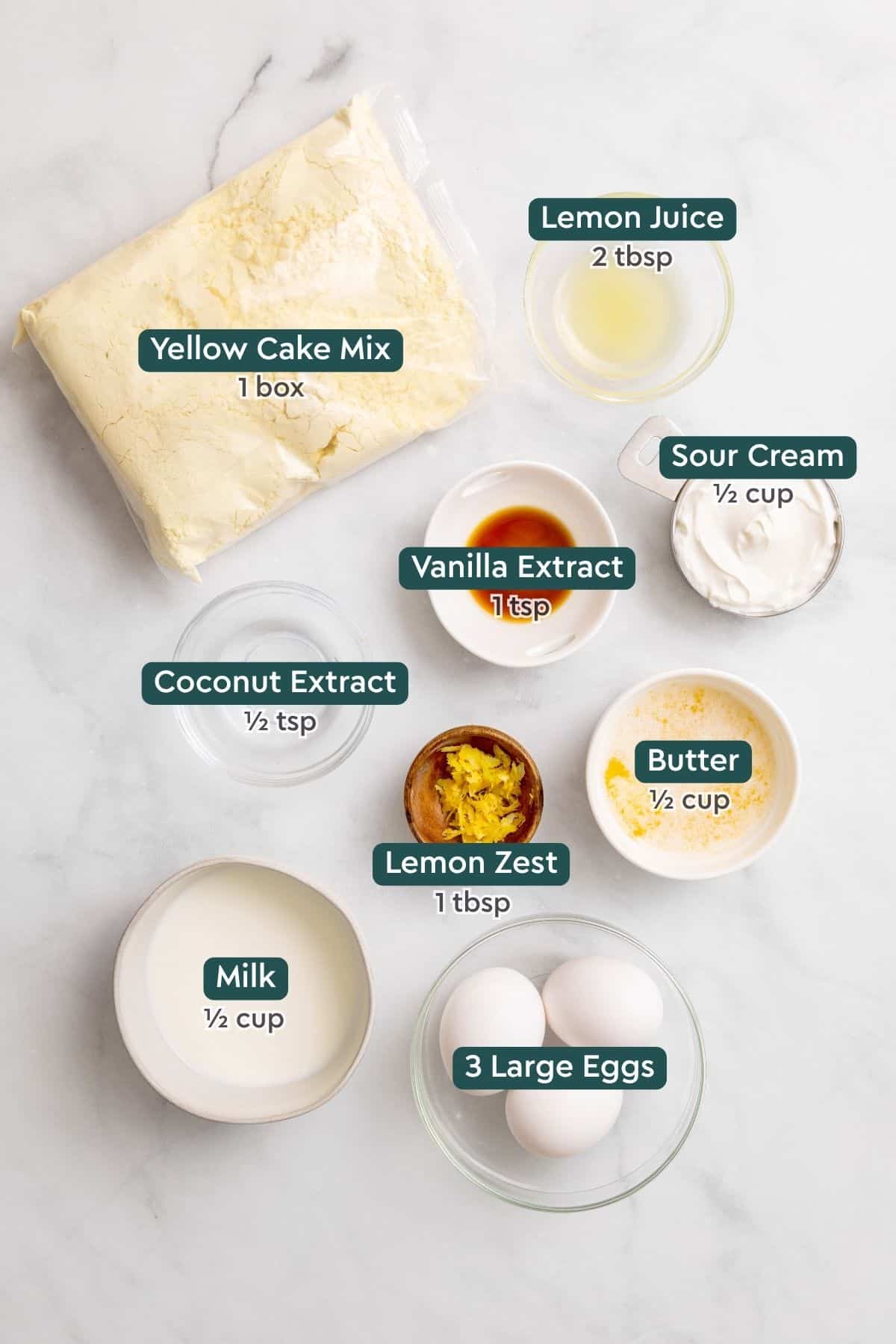 Ingredients for lemon coconut cake, including cake mix, lemon, sour cream, vanilla, coconut extract, butter, milk, eggs.