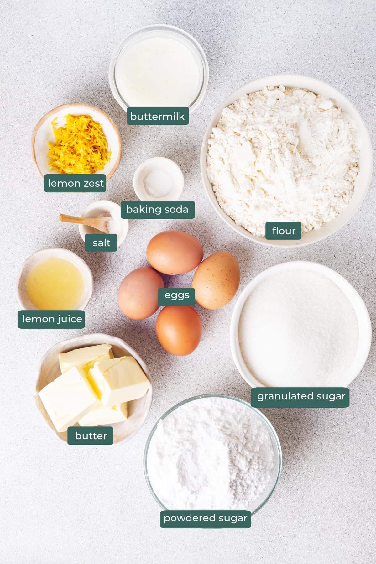 All of the ingredients for lemon bundt cake in bowls on a white countertop.