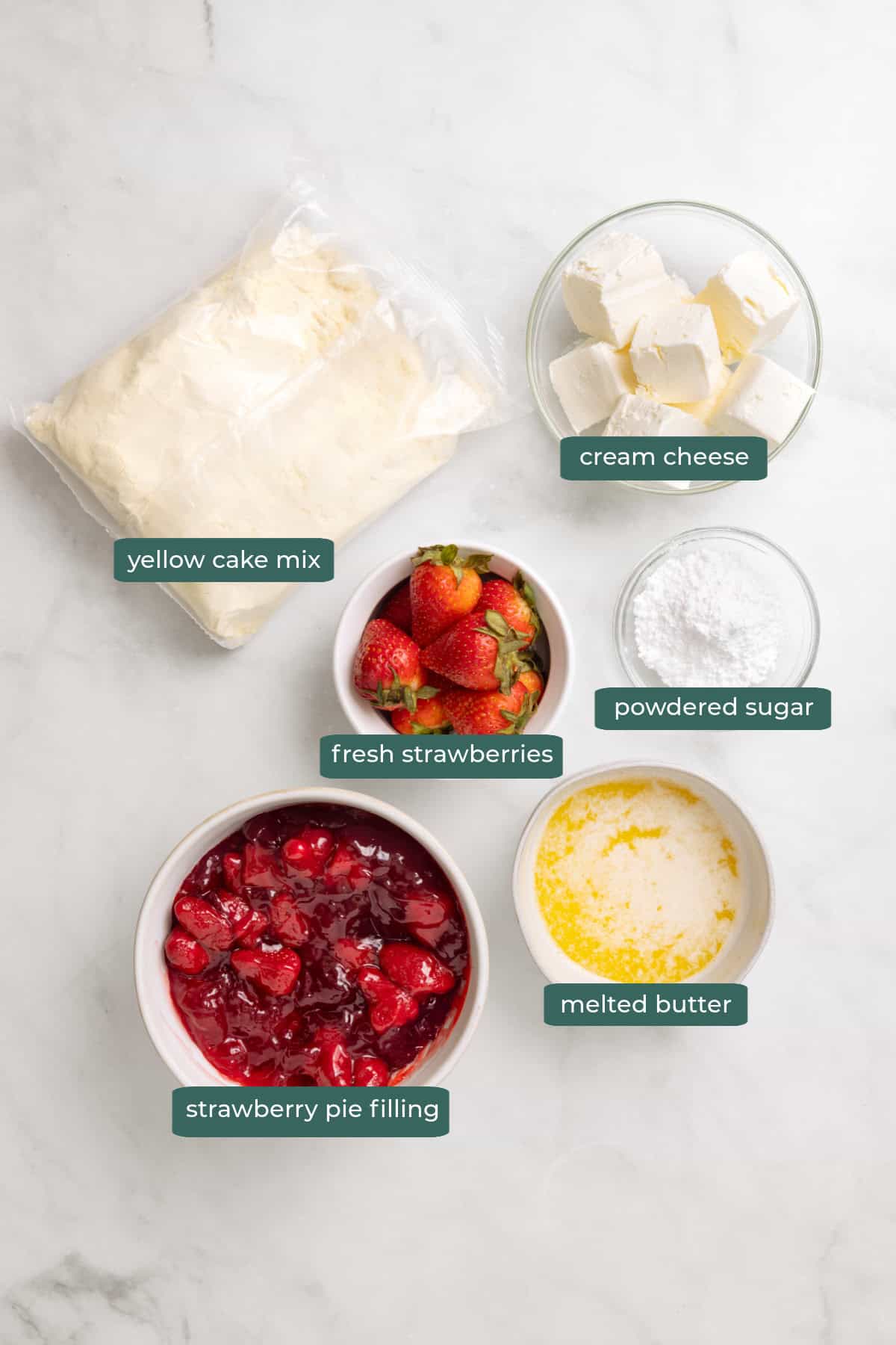 All of the ingredients for strawberry cheesecake dump cake in bowls on a white countertop.