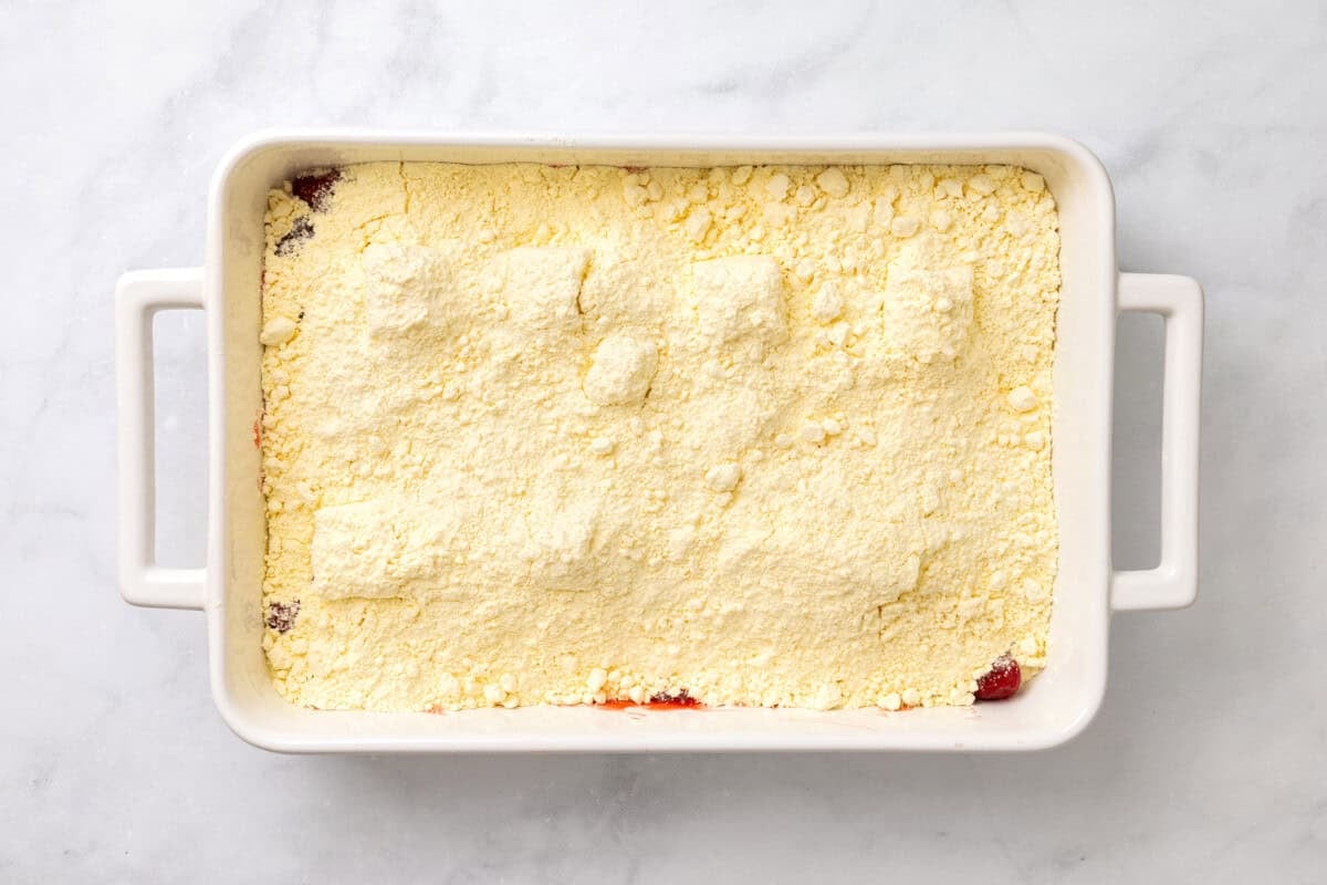 Cake mix added to pan for strawberry cheesecake dump cake.