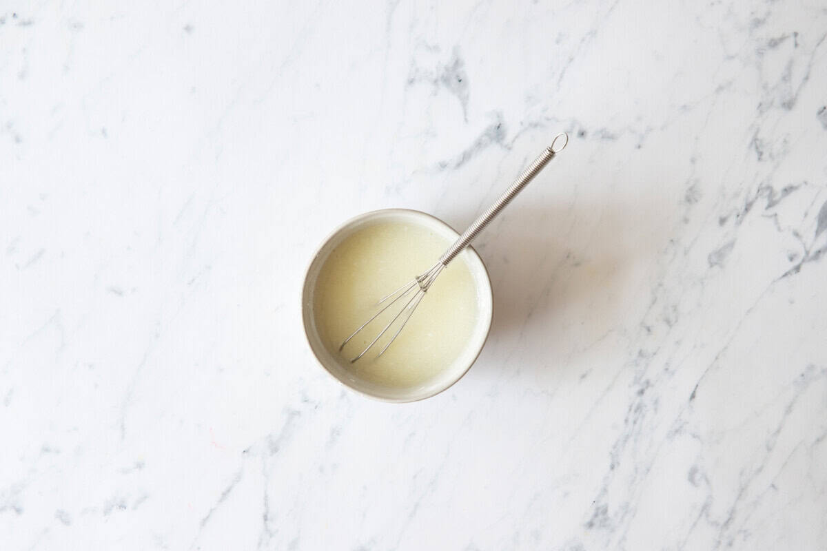 Lemon glaze in bowl with whisk.