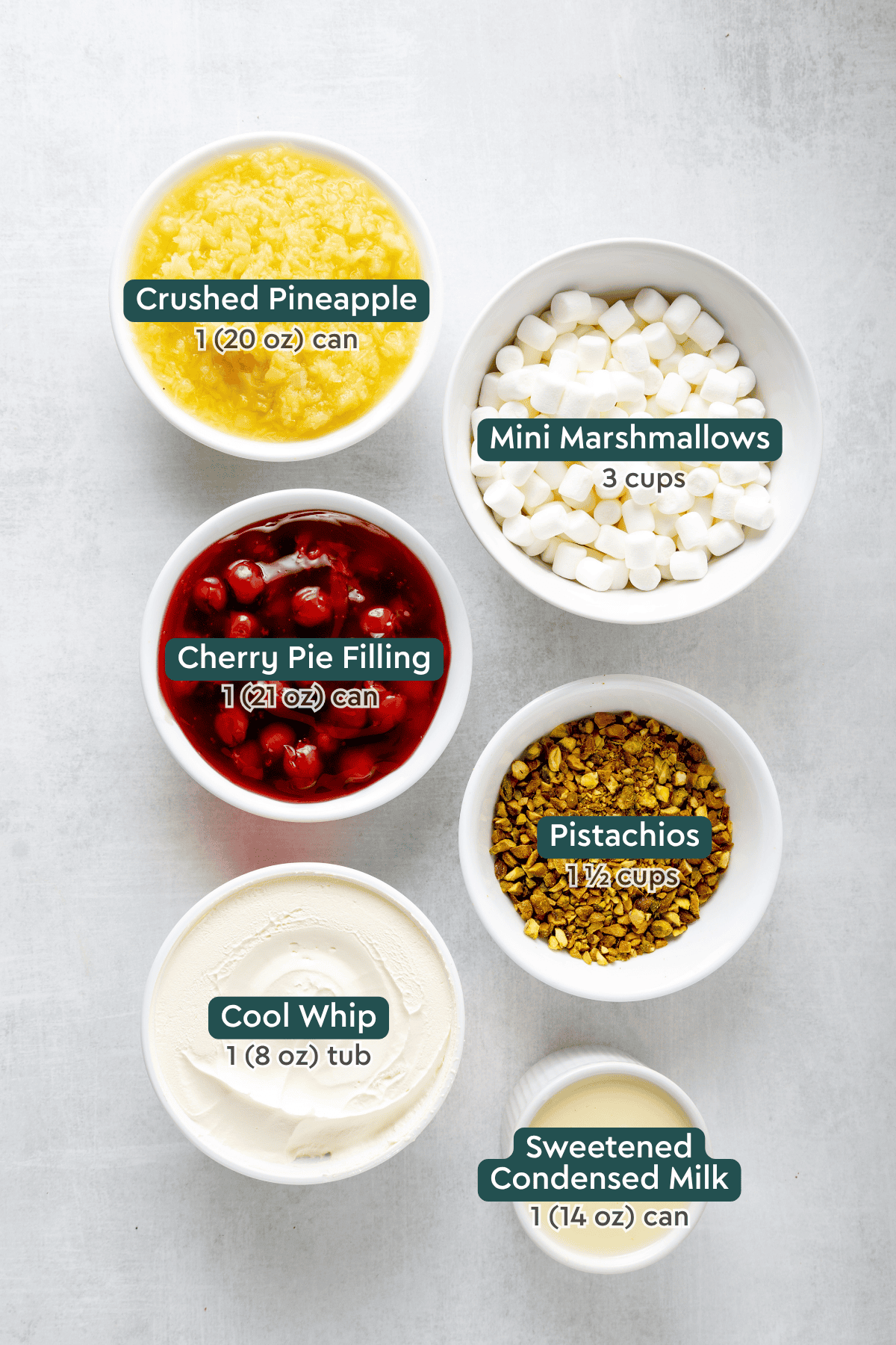 All of the ingredients for Cherry Fluff Salad in bowls on a white countertop.