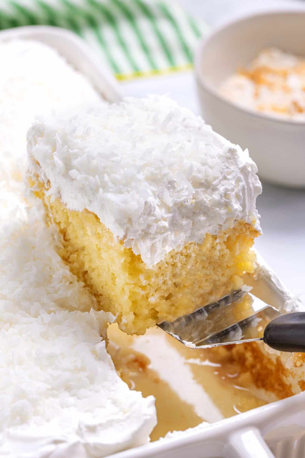 Coconut poke cake coming out of a cake pan on a spatula. 