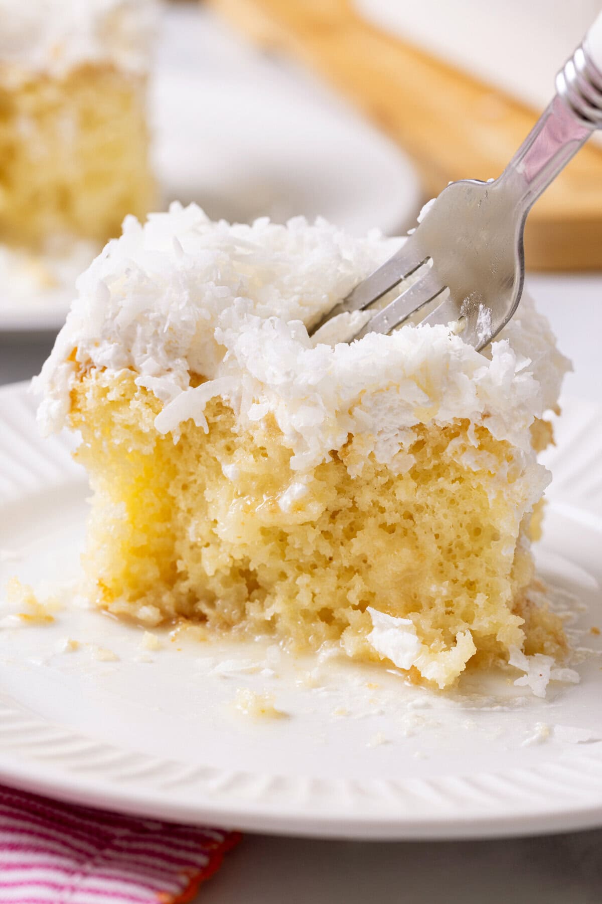 fork cutting into a slice of coconut poke cake made with cake mix. 