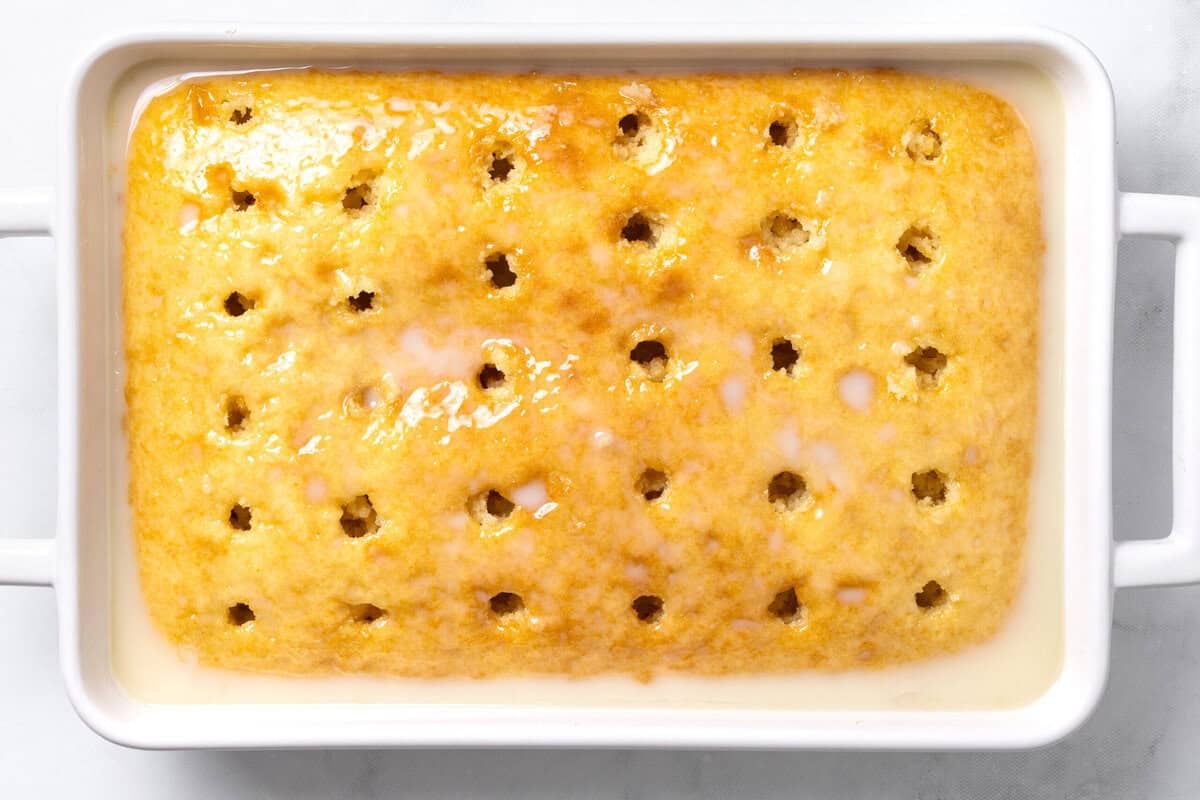 top down view of 9x13 baking dish with baked vanilla cake and holes poked in the cake.