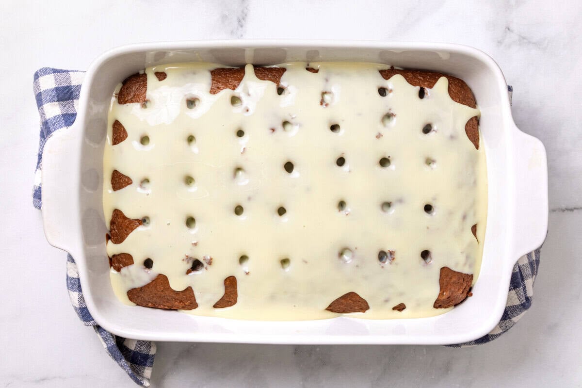 Condensed milk poured over chocolate cake in pan.