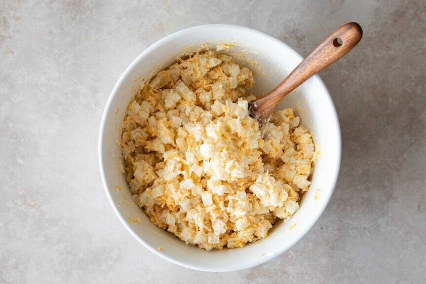 cheesy potato mixture in bowl with wooden spoon.