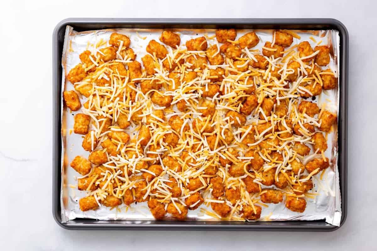 Step 2 to make loaded tater tots: sprinkle shredded cheese over the pre-baked tater tots.