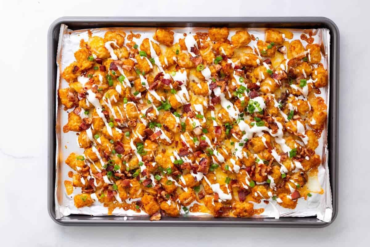 Step 4 to make loaded tater tots: top with chopped bacon pieces, sliced green onion, and sour cream.