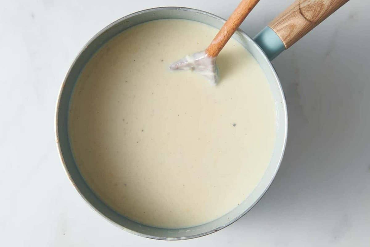 Wooden spoon stirring cheese sauce in pan.
