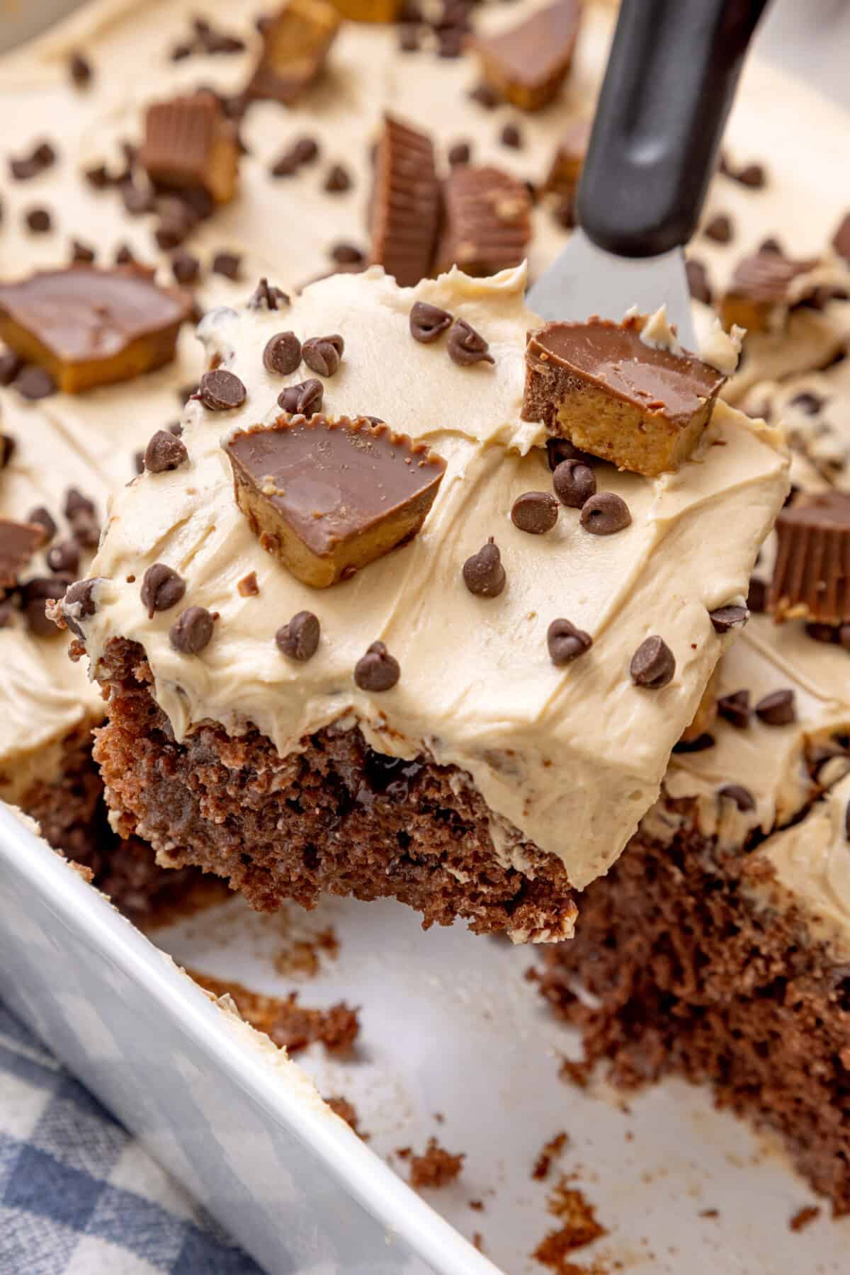 Spatula lifting slice of chocolate peanut butter poke cake from pan.