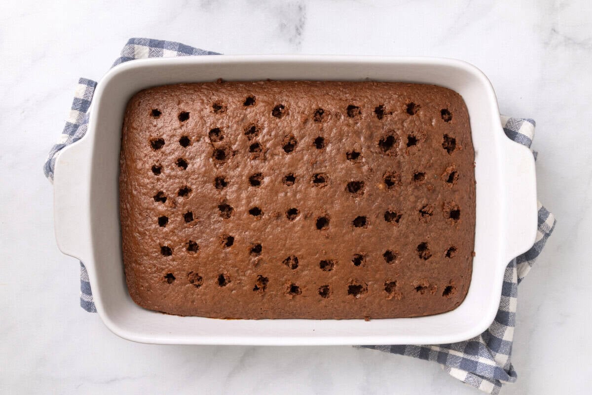 Chocolate cake in pan with holes poked throughout.