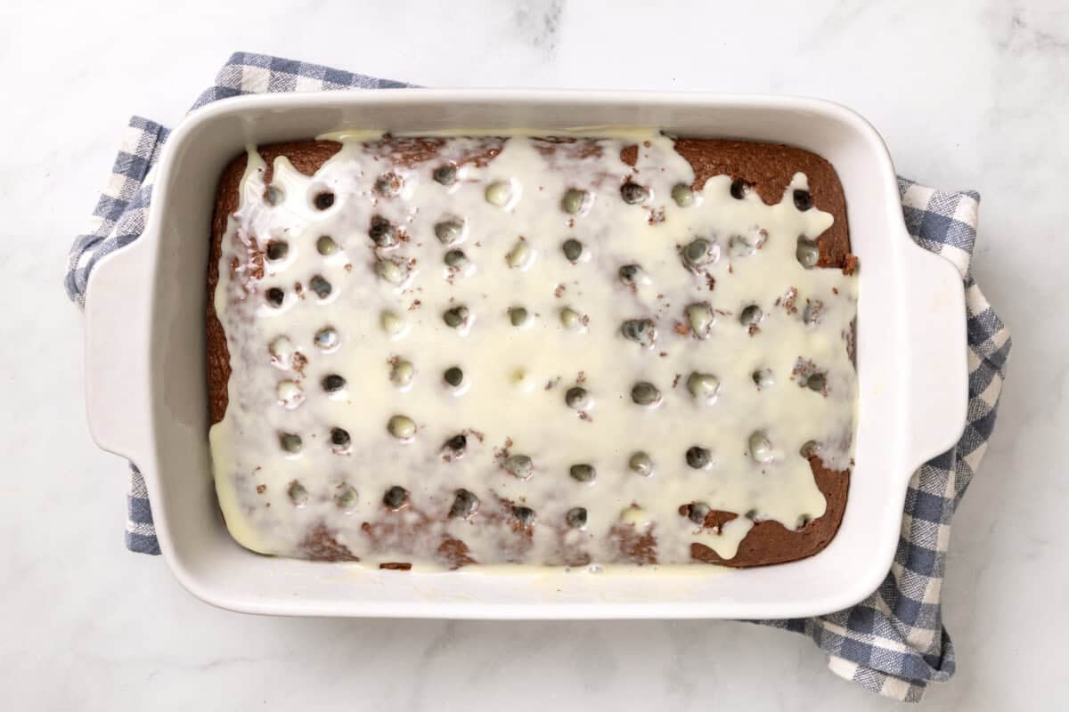 Sweetened condensed milk spread over chocolate cake in pan.