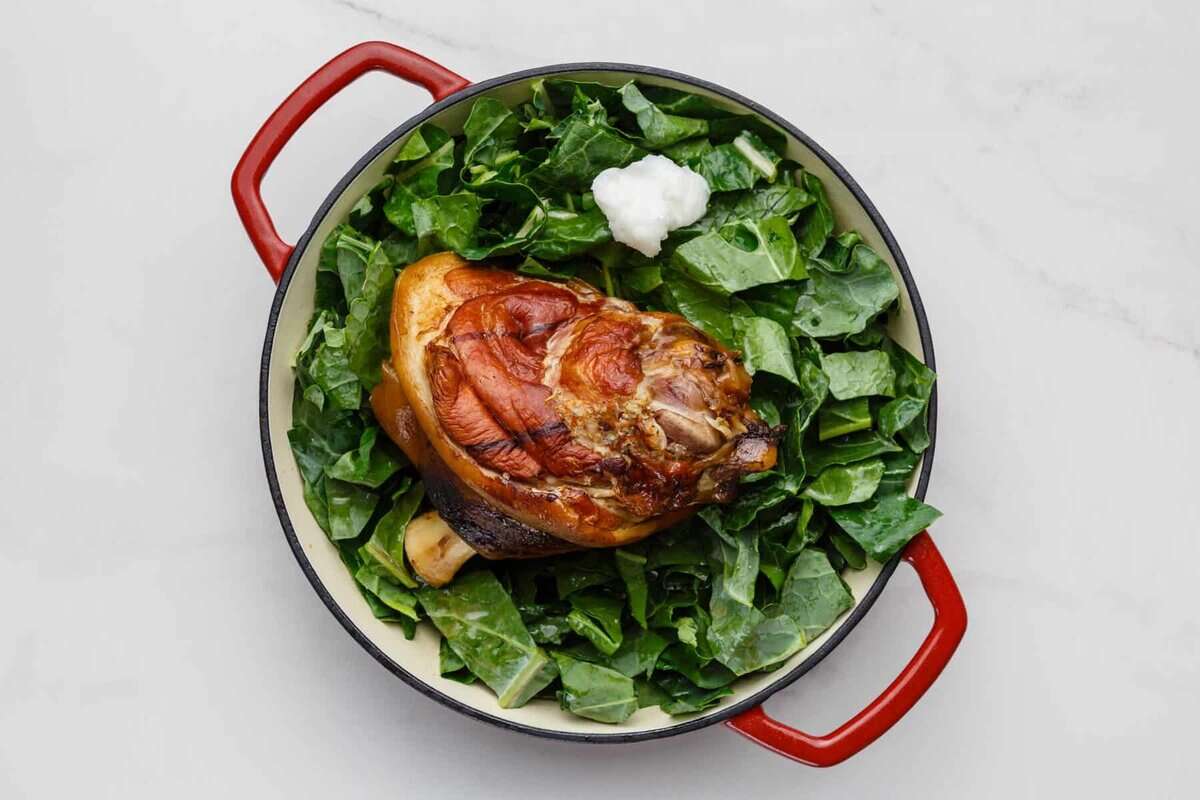 Collard greens and ham hocks cooking in a white Dutch oven. 