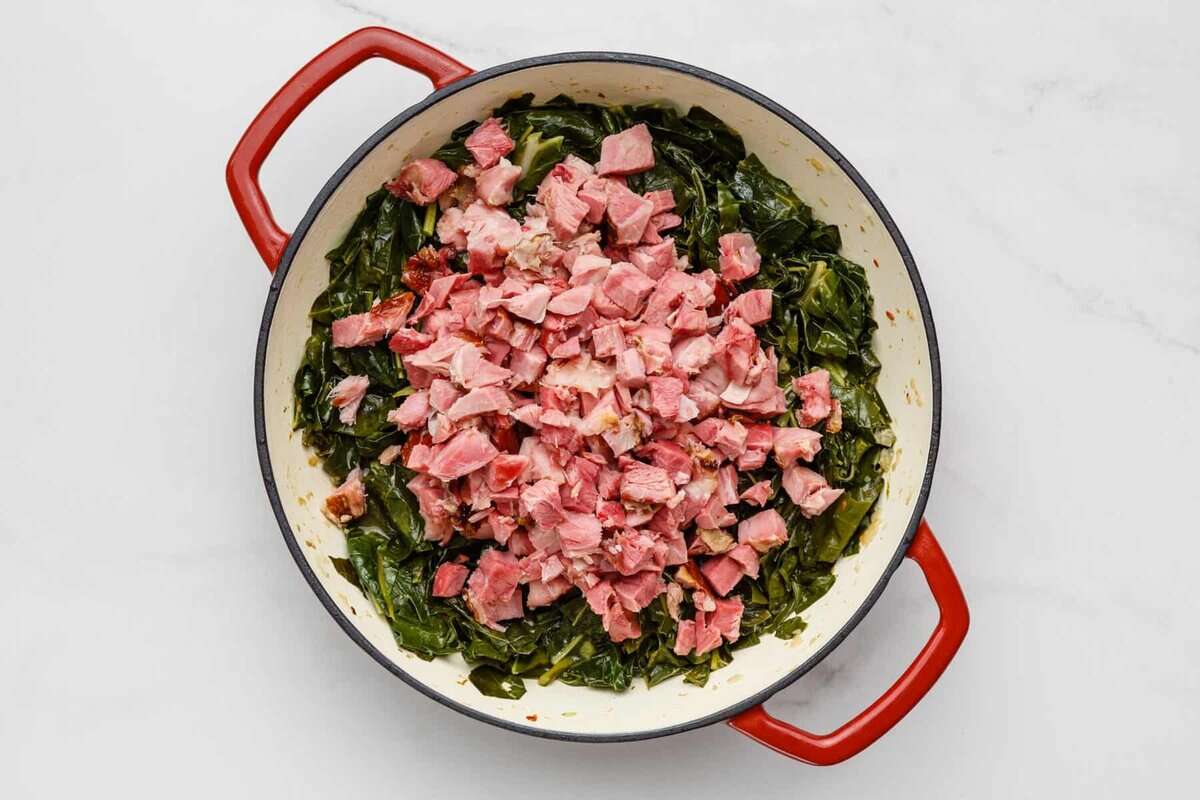 Collard greens and bacon cooking in a white Dutch oven. 