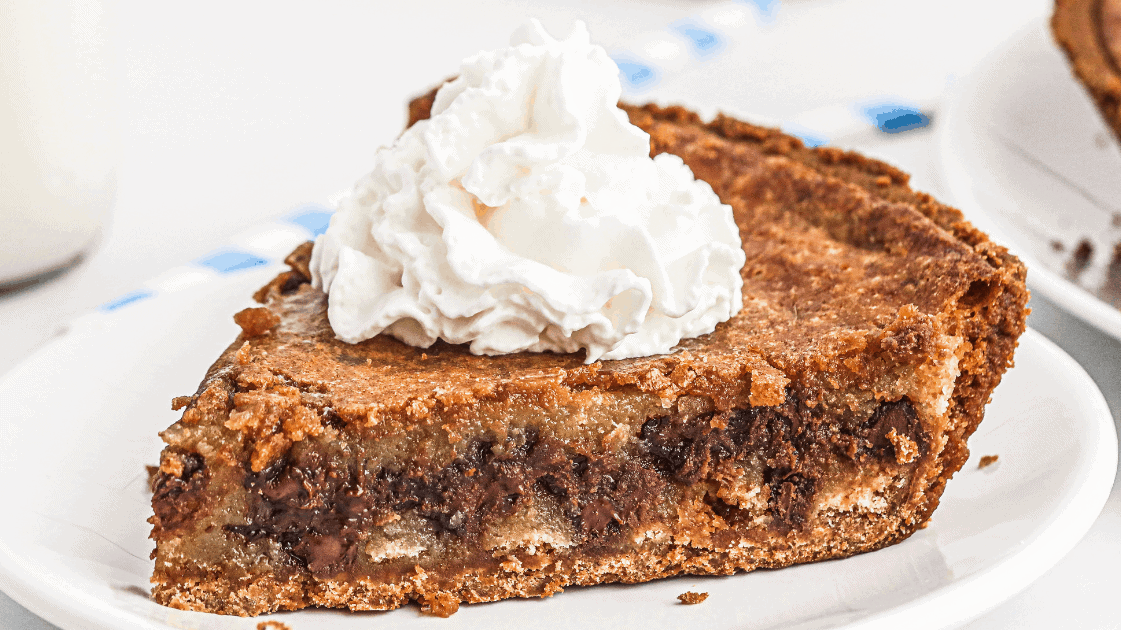 slice of chocolate chip pie with a swirl of whipped cream on top served on a white plate