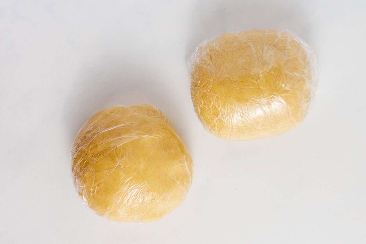 Two balls of pie crust dough wrapped in plastic.