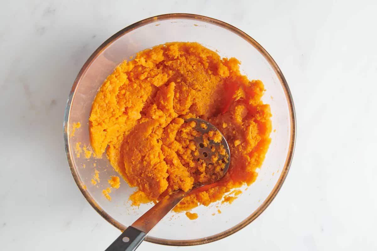Mashing sweet potatoes in glass bowl.