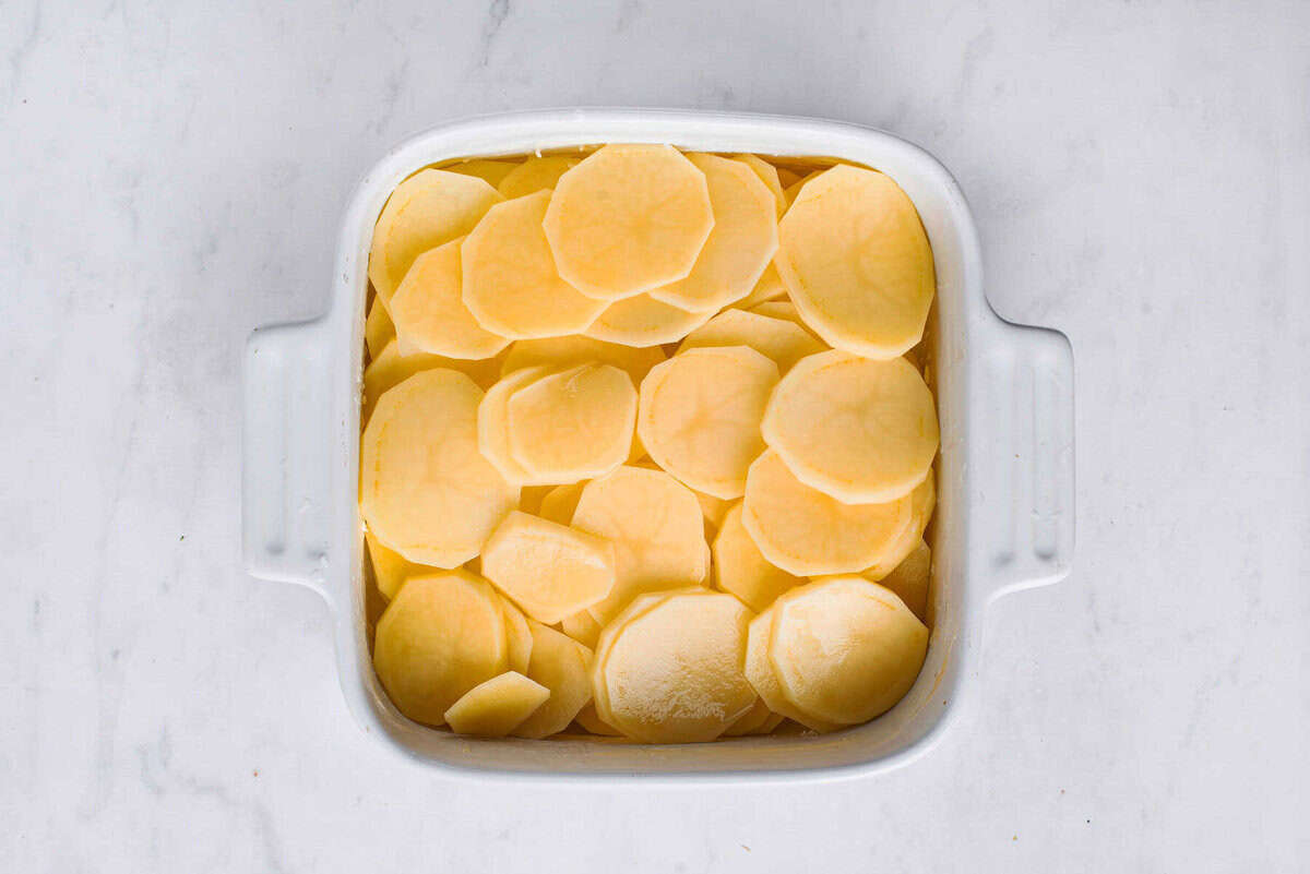 The sliced potatoes layered in a square baking dish before adding the sauce.