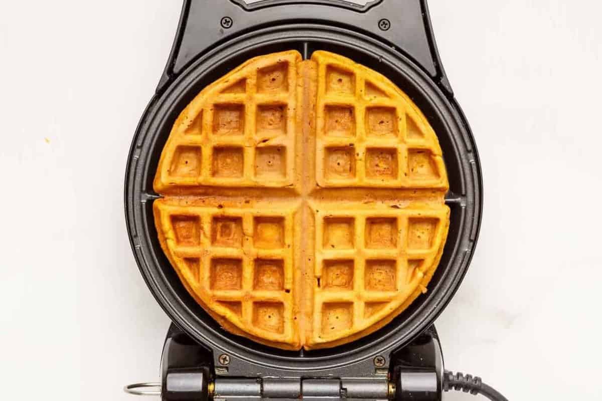 A sweet potato waffle cooking in a waffle maker. 