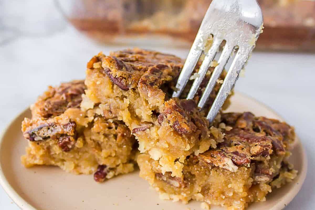 Pecan pie bars on a white plate with a fork taking a piece.