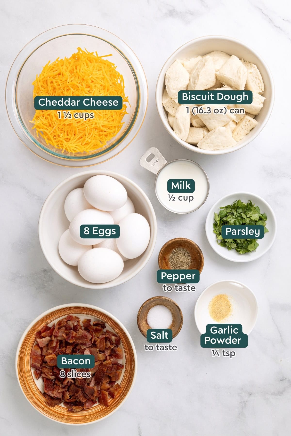 Ingredients for biscuit casserole including cheese, biscuit dough, milk, eggs, parsley, pepper, salt, garlic powder, and bacon.