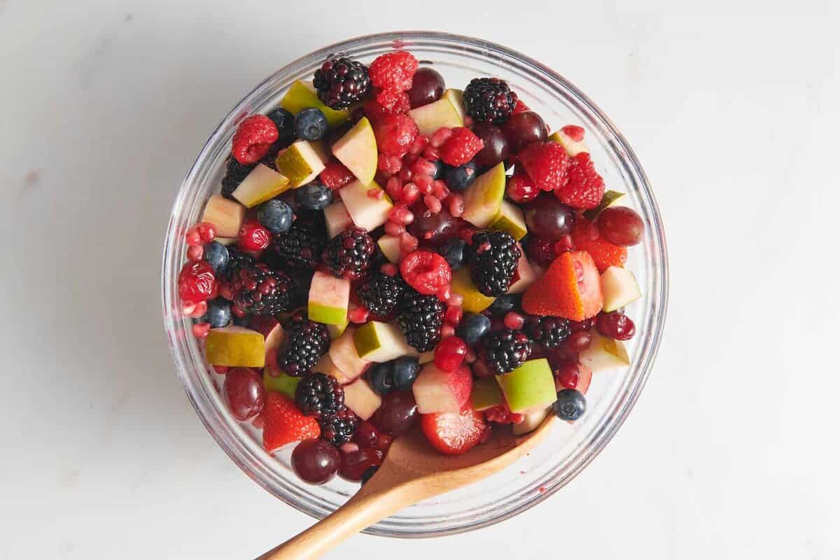 Fruit in large glass bowl with wooden spoon.