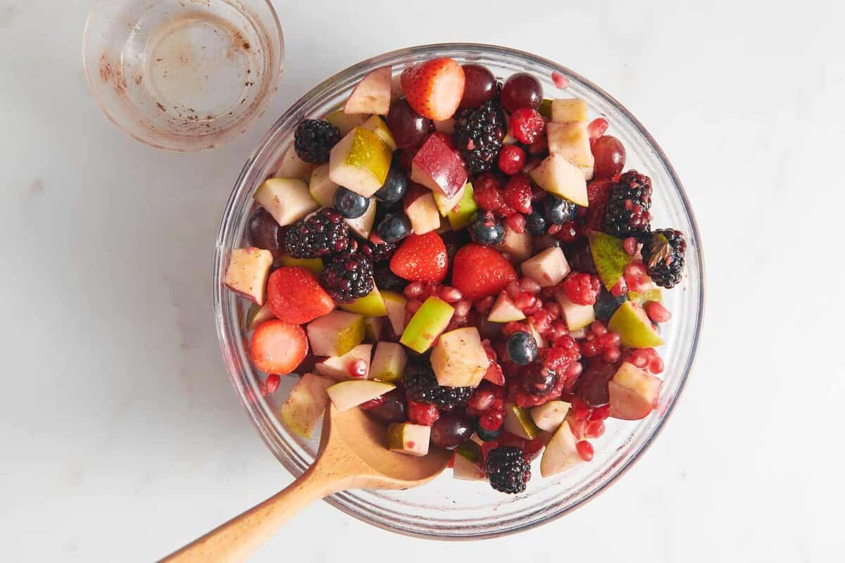 Christmas fruit salad in bowl with wooden spoon.