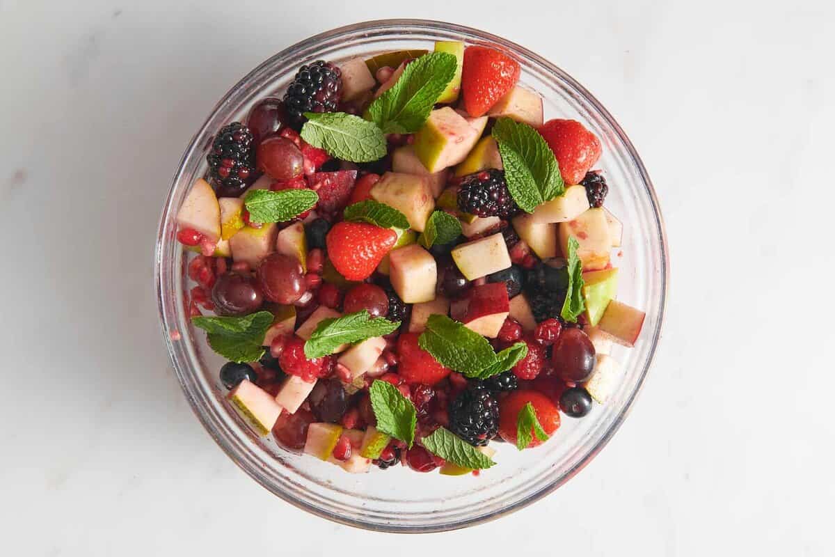 Mint leaves added to bowl of Christmas fruit salad.
