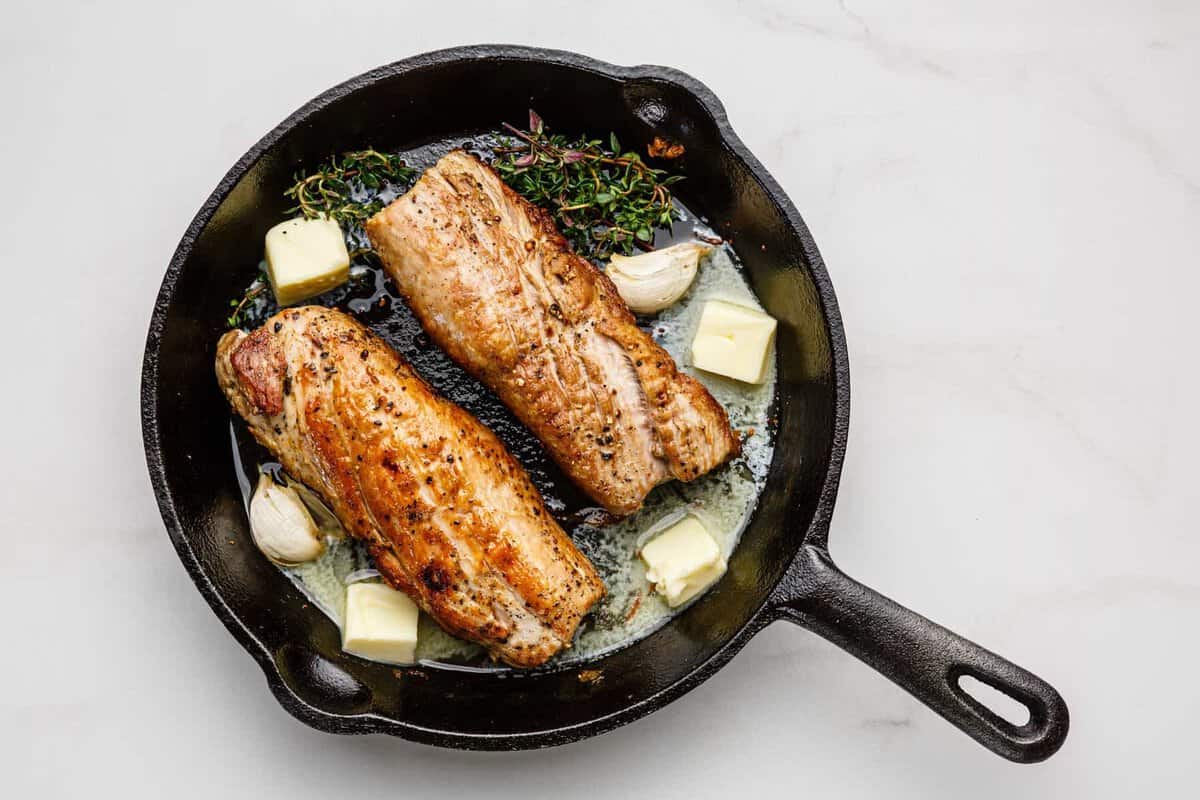 Pork tenderloins in skillet with butter and herbs.
