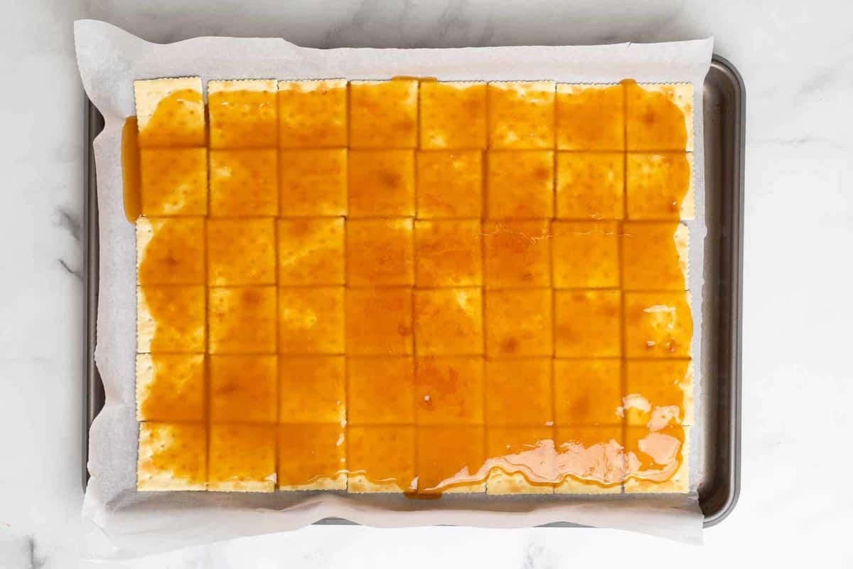 Toffee mixture spread over saltine crackers on sheet pan.