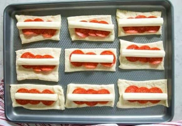 Pizza dough topped with pepperoni and string cheese.