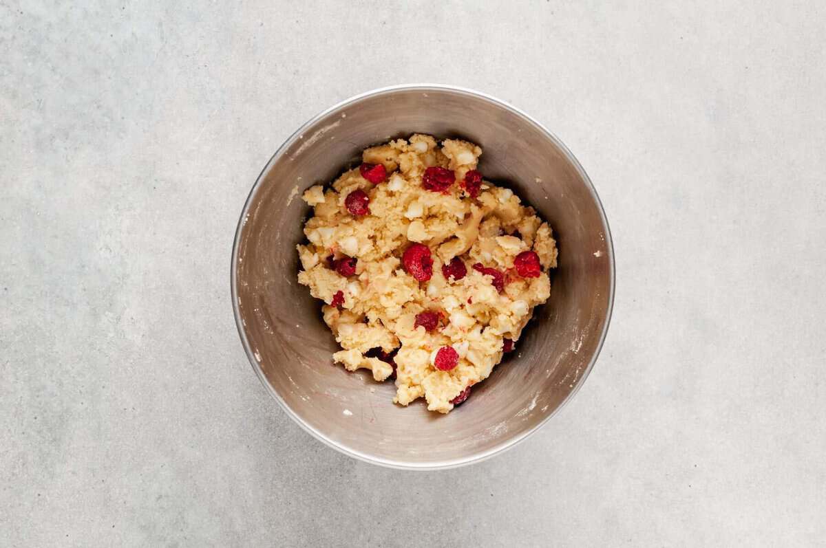 Raspberries and white chocolate chips folded into bowl of cookie dough.